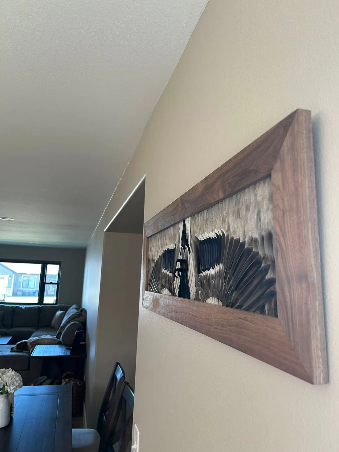 A mallard flying mount in a walnut frame hanging in a hallway that opens to the living room